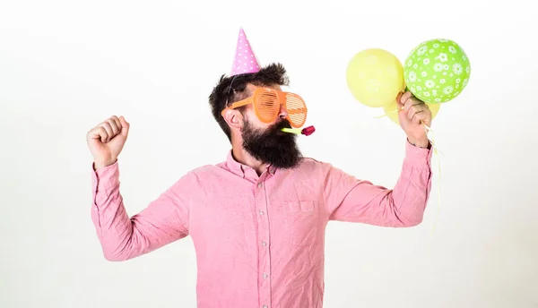 Killen i partiet hatt med air ballonger firar. Mannen med skägg och mustasch på upptagen ansikte blåser in part horn, vit bakgrund. Celebration koncept. Hipster i giant solglasögon firar födelsedag — Stockfoto