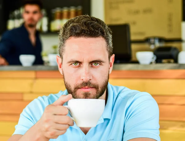Man bearded serious face needs energy charge. Caffeine makes you more energetic. Serious guy enjoy caffeine drink close up. Start day with big cup of coffee. Traditional coffee break cafe background