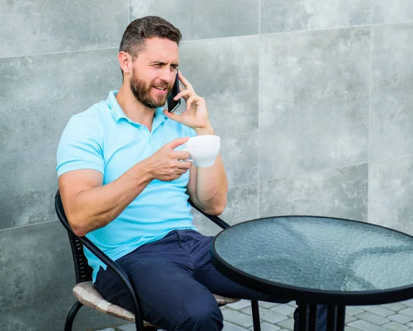 Descanso de café trae bienestar físico y mental. Es hora de relajarse. Breve descanso café proporciona a los empleados con formas rápidas de relajarse. Hombre sentarse terraza y beber cappuccino hablar teléfono gris pared fondo — Foto de Stock