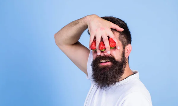 Dream of strawberry. Man bearded hipster hold hand with strawberries in front of eyes. Glance of man blocked by berries. Strawberry on my mind. Man can not see anything but strawberry blue background