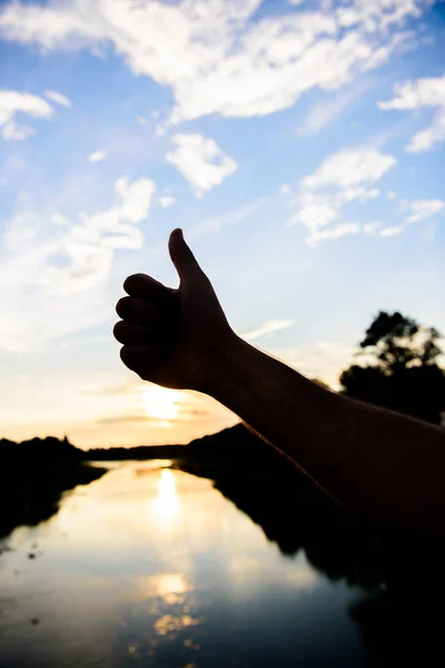 Pulgares hacia arriba signo de gesto de la mejor opción aprobar y aceptar. Silueta pulgar hacia arriba gesto delante de la puesta de sol sobre la superficie del agua del río. Atardecer luz del sol ambiente romántico. Los mejores lugares para visitar en la noche —  Fotos de Stock