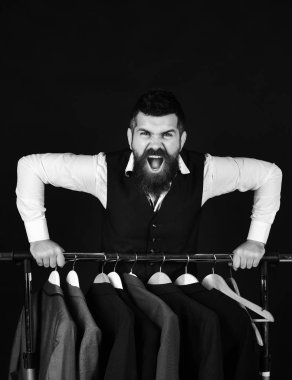 Elbise rafında sakallı bir adam. Öfkeli yüzlü bir iş adamı.