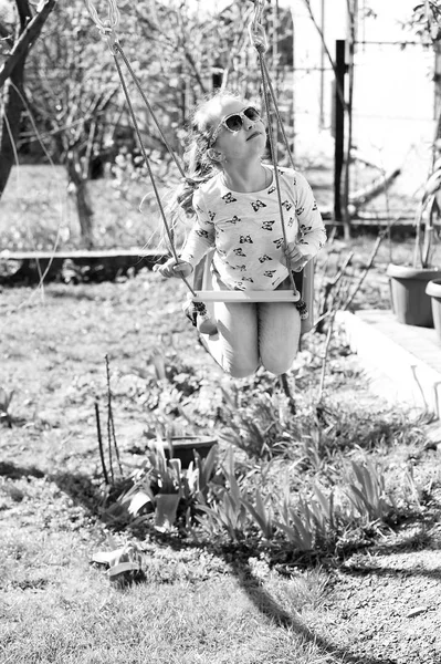 Güneş gözlüklü moda kızı güneşli bir günde sallanmaktan hoşlanır. Küçük çocuk yaz bahçesinde salıncakta sallanıyor. Çocuk parkındaki güzel çocuk. Mutlu çocukluk kavramı. Özgürlük tasasız yaşam tarzı ve eğlence — Stok fotoğraf
