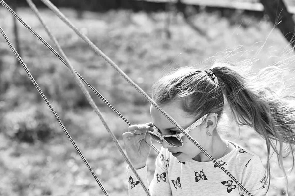 Freiheit, unbeschwerter Lebensstil und Spaß. Modemädchen mit Sonnenbrille schwingen gerne an sonnigen Tagen. Kleines Kind auf Schaukel im Sommergarten. Schönheitskind auf dem Spielplatz. Glückliche Kindheit — Stockfoto