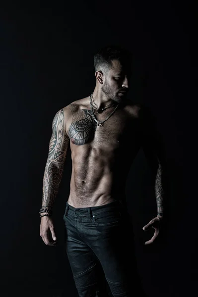 Modelo de moda com tatuagem em jeans. Homem tatuado mostra torso muscular sexy. Esportista com seis maços e abdominais. Fisiculturista com bíceps e tríceps. Cuidado com o corpo com fitness e esporte no filtro vintage — Fotografia de Stock