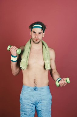 Çıplak gövdeli bir adam havluyu boynunda ve dambıllarında tutuyor.