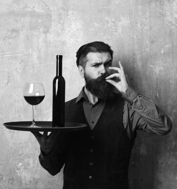 Sakallı adam bej duvar arkasında şarap tutuyor.