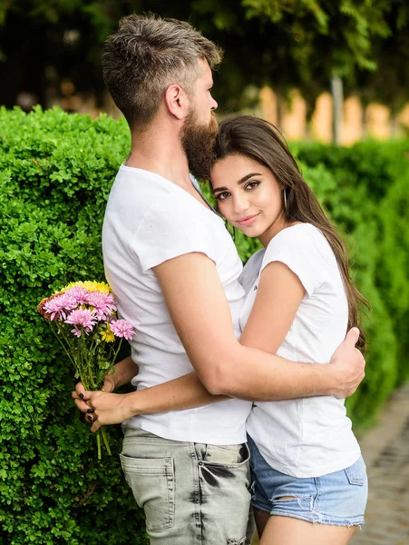 Hombre barbudo hipster abraza a mujer. El hombre se enamora de una chica preciosa. Los fuertes sentimientos románticos se convierten en amor verdadero. Ella conquistó su corazón. Pareja en amor abrazos en fecha en parque verde arbustos fondo —  Fotos de Stock