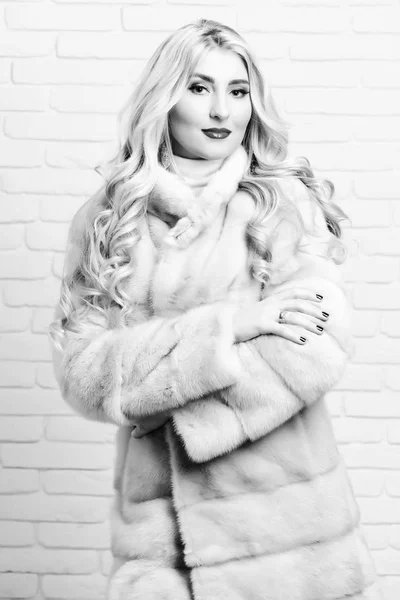 Young fashionable sexy pretty woman with beautiful long curly blonde hair in waist coat of beige fur and fashion makeup on brick wall studio background. — Stock Photo, Image