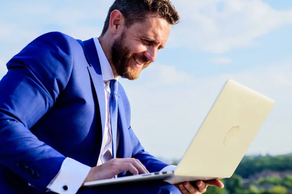 Businessman surfing internet or reply emails while sit with laptop outdoors. Increase online reputation tips. Online reputation of your brand. Social media marketing expert works blue sky background