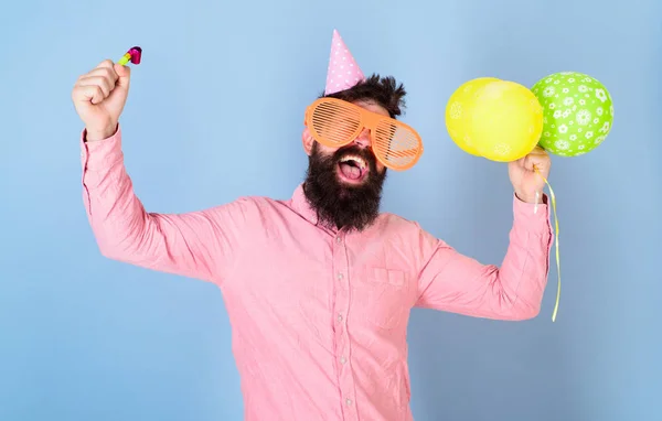 Mann mit Bart und Schnurrbart auf glücklichem Gesicht hält Luftballons, hellblauer Hintergrund. Hipster mit Riesenbrille feiern Geburtstag. Parteikonzept. Mann im Partyhut mit Urlaubsattribute feiert — Stockfoto
