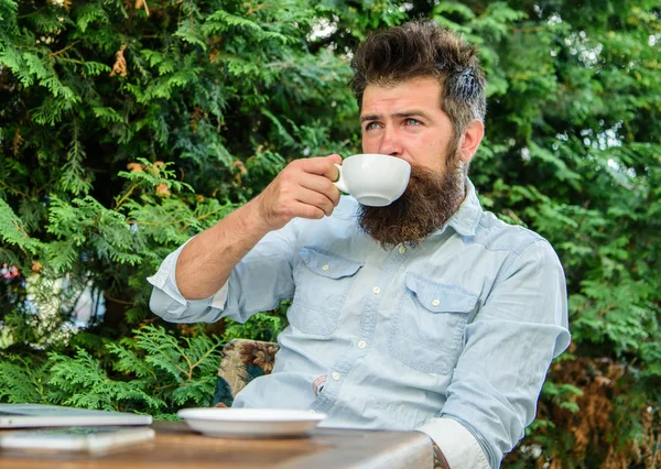 Take moment to enjoy life. Man bearded hipster make pause for drink coffee and relax while sit with laptop. Guy drinks coffee relaxing terrace branches background. Aroma cappuccino. Pleasant moment