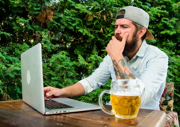 Brutal man leisure with beer and sport game. Championship stream online. Football fan bearded hipster watch game on laptop screen. Fan watch stream online while sit terrace outdoors with beer mug