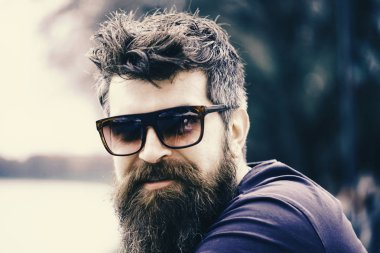 Nehir setin arka plan üzerinde giyer gözlüklü, sakal ve bıyıklı adam. Hippi moda güneş gözlüğü ile kendine güvenen yüzünde. Erkek moda kavramı. Adam ile şık güneş gözlüğü emin görünüyor