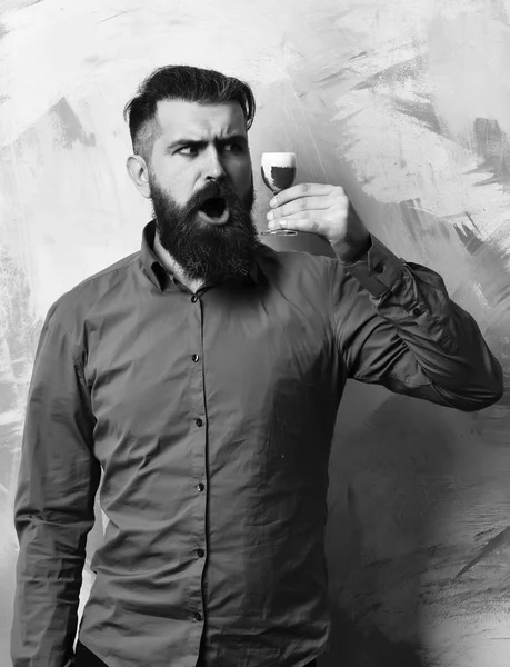 Bearded man, long beard. Brutal caucasian surprised hipster with moustache in brown shirt holding alcoholic red shot on colorful texture background. — Stock Photo, Image