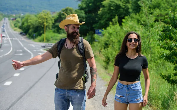 Pár utazó férfi és a lány stoppolás edge road természet háttér. Utazók próbálja megállítani az autót. Pár stopposok utazik a nyári napsütésben. Autóstoppal az egyik legolcsóbb ways-ból utazótáska — Stock Fotó