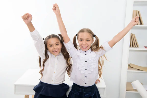 Gelukkige leerlingen houden elkaars handen omhoog in het klaslokaal, overwinningsconcept. Kleine meisjes vieren de overwinning. Wij zijn de winnaars. gelukkig kleine meisjes. — Stockfoto