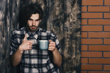 Duvarda bardağı tutan yakışıklı adam ve tahta arka plan.