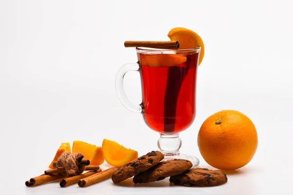 Autumn beverage concept. Drink or beverage with cinnamon sticks, orange fruit and cookies with chocolate drops. Glass with mulled wine or drink near juicy orange fruit on white background, close up — Stock Photo, Image