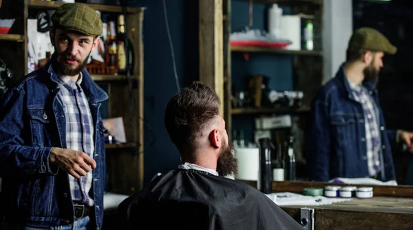 Fryzjer i hipster klienta z brodą sprawdzanie fryzura w lustro, ciemne tło. Człowiek z brodą wyjaśnić fryzurę, którą preferuje. Hipster i mówi podczas sesji strzyżenie Fryzjer. Pojęcie usługi — Zdjęcie stockowe