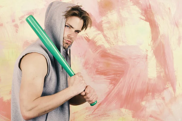 Guy in grey sleeveless hoodie holds bright green bat