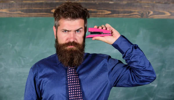 Hipster nauczyciel wizytowym z szyi krawat posiada zszywacz. Powrót do szkoły i studia. Nauczanie techniki pamięciowe. Nauczyciel Brodaty mężczyzna z różowy zszywacz tablica tło. PIN to na uwadze — Zdjęcie stockowe
