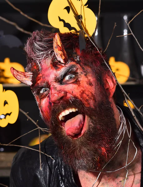 Man wearing scary makeup with Halloween pumpkins and bats decor