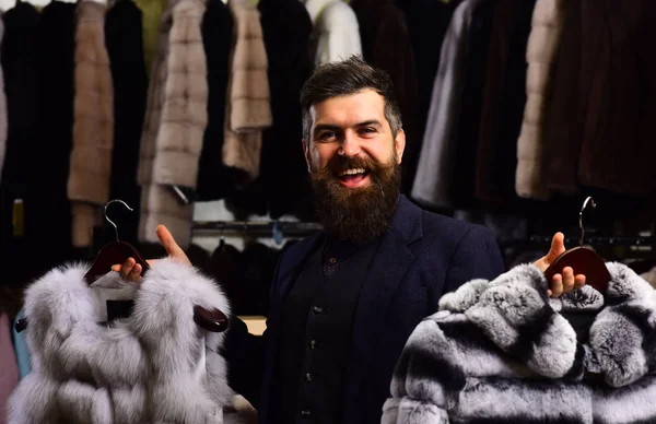 Chico con cara feliz muestra abrigos de piel en tienda de moda . — Foto de Stock