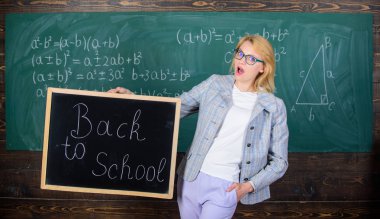 Öğretmen yeni öğretim yılı ağırlamaktadır. Yeni okul sezon başında. Kadın öğretmen resmi elbise blackboard yazıt okula geri tutar. Bayan eğitimci sınıfta yeni öğretim yılı için hazırlamak