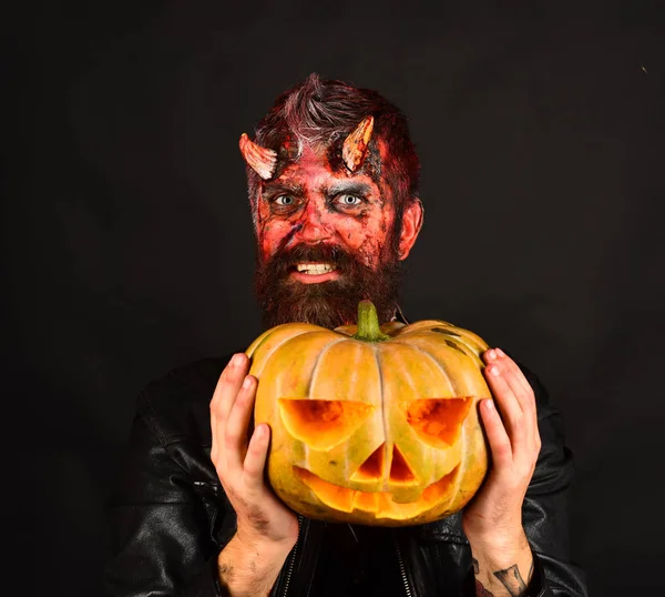 Man wearing scary makeup holds pumpkin on black background