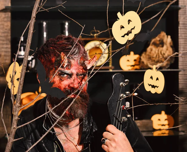 Man wearing scary makeup behind Halloween pumpkins and bats decor