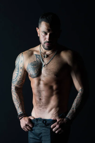 Sportsman con sei pack e addominali stripping. Uomo spogliarellista mostra busto sexy. Atleta con muscoli bicipiti e tricipiti. Uomo di moda con tatuaggio decollare jeans. Desiderio di sessualità e attrazione — Foto Stock