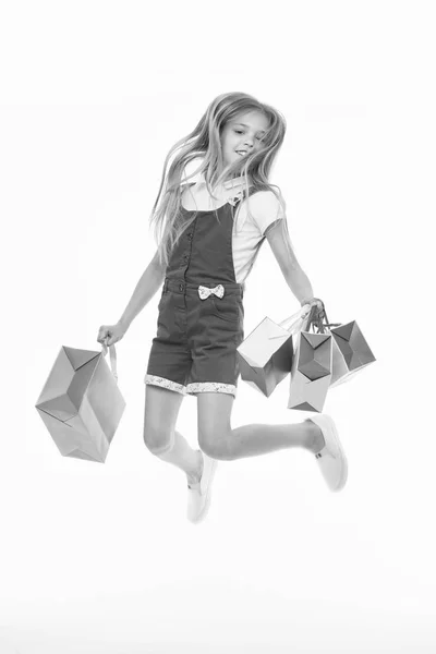 Happy child jump with shopping bags isolated on white. Little girl smile with paper bags. Kid shopper in fashion jumpsuit. Holidays preparation and black friday. Shopping therapy makes her happy.