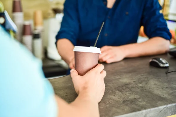 Hand of barista at bar serve coffee for client. Hand gives cup to client visitor. Enjoy your drink. Man receive drink at bar counter. Cappuccino or cacao with straw. Served in paper cup coffee to go — Stock Photo, Image