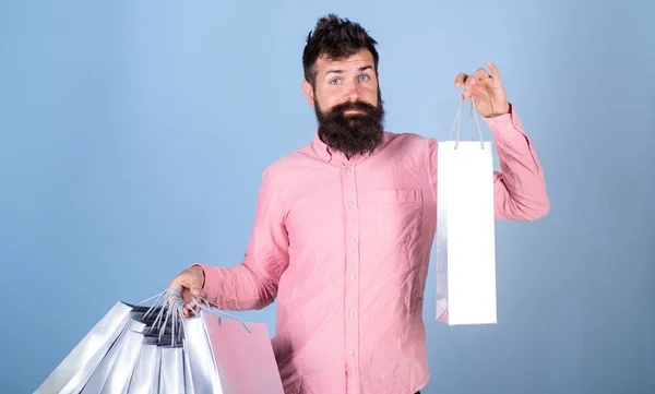 Sale and discount concept. Hipster on smiling face carries shopping bags. Man with beard and mustache works as shop assistant, light blue background. Guy shopping on sales season with discounts — Stock Photo, Image