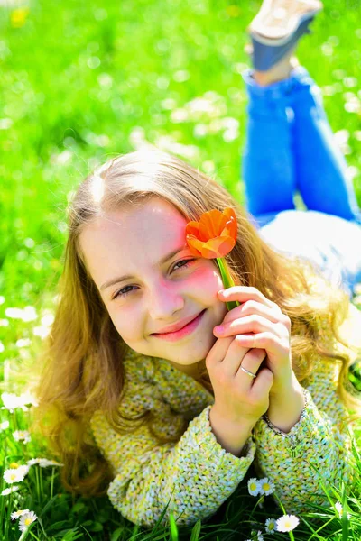 笑顔の女の子が赤いチューリップの花を保持して、香りをお楽しみください。背景に草地の草の上に横たわる少女。子供では、春の晴れた日、花と草原で横になってお楽しみください。若さと屈託のないコンセプト — ストック写真