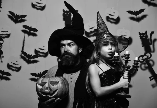 Wizard and little witch in black hats hold pumpkin