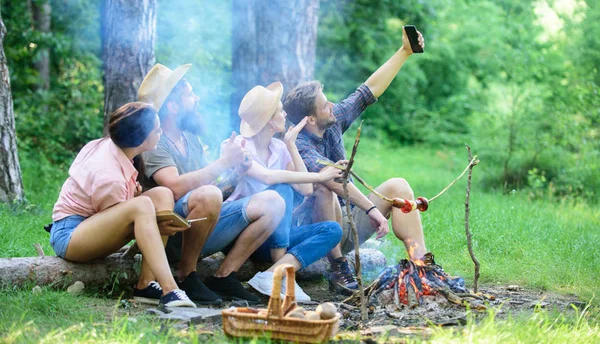 Tourists sit log near bonfire taking photo on smartphone. Friends on vacation capture moment. Man taking photo near bonfire nature background. Friends near bonfire enjoy vacation and roasted food