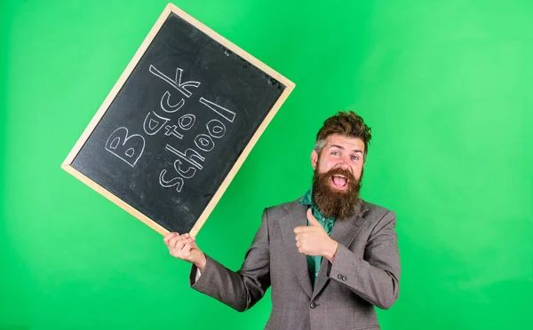 Professeur barbu homme tient tableau noir avec inscription retour à l'école fond vert. Enseignant heureux joyeux félicite avec le début de la nouvelle année scolaire. Inviter à célébrer le jour de la connaissance — Photo