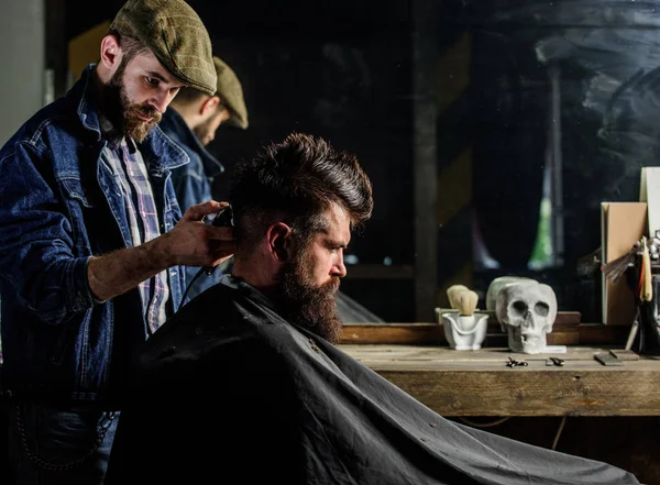 Парикмахер укладывает волосы жестокого бородатого клиента с клиппером. Концепция образа жизни хипстеров. Клиент хипстера стрижется. Парикмахер с клиппером работает над прической для бородатого человека парикмахерского фона — стоковое фото
