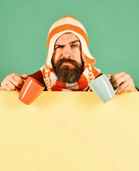 Hombre en sombrero caliente sostiene tazas de color naranja y azul —  Fotos de Stock