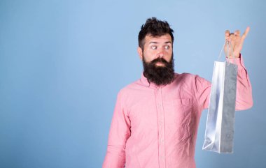 Heyecanlı yüz bağımlısı alışveriş veya Alışverişkoliğin hippi. Satış sezon indirimlerle alışveriş adam. Adam sakal bakışla alışveriş çantası, açık mavi renkli, uzay kopyalayın. Satış ve indirim kavramı