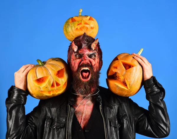 Man wearing scary makeup holds pumpkins on blue background