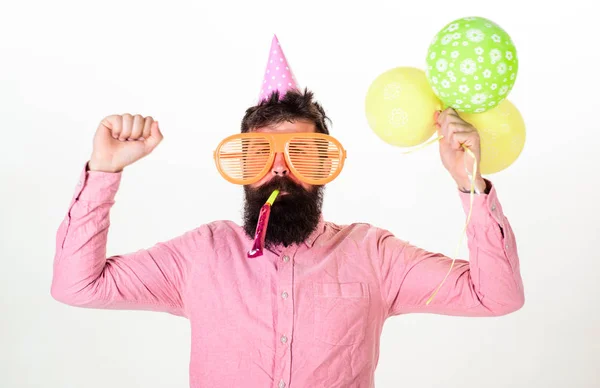 お祝いのコンセプトです。ひげと口ひげをつけたパーティー角、白い背景に忙しい顔吹く男。空気風船でパーティー帽子の男を迎えます。誕生日を祝って巨大なサングラスで流行に敏感な — ストック写真