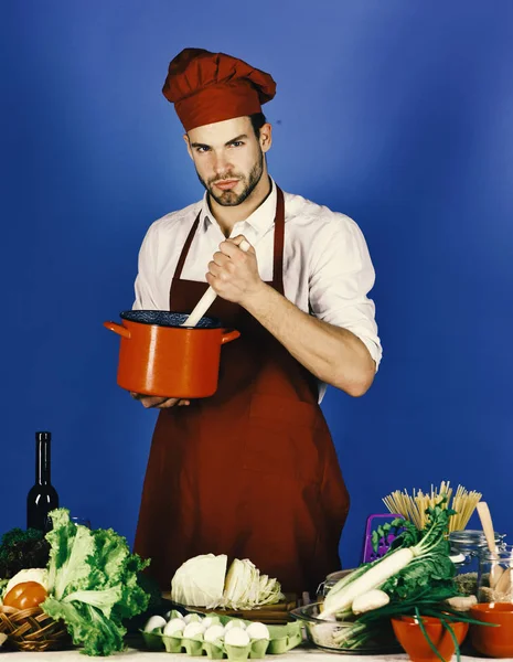 Man in cook uniform mixes in pot with wooden spoon