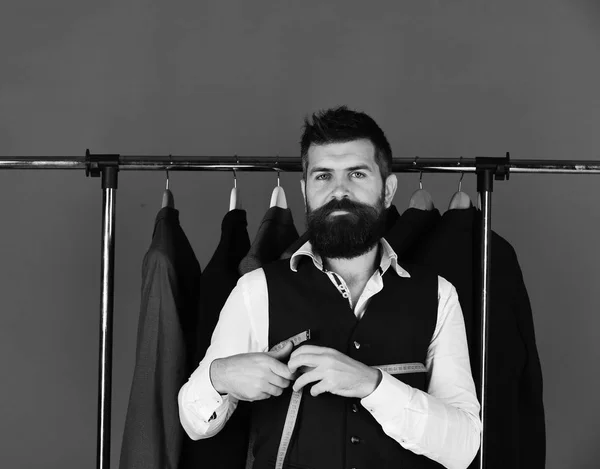 Man with beard by clothes rack. Tailor with serious face