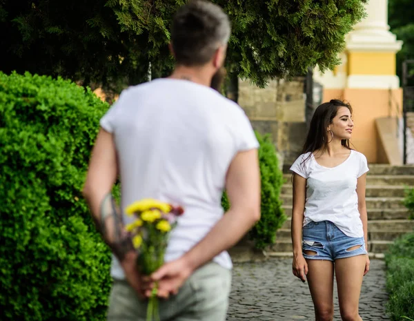 First impression always important. Surprise for her. Man hides flower bouquet behind back waits romantic date. Dating tips that will transform your love life. Couple meeting for date park background