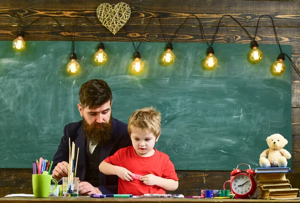 Çocuk ve öğretmen meşgul yüzleri boyuyor, resim çiziyor. Sakallı öğretmen, baba ve küçük oğlu sınıfta resim çizerken, yaratırken, arka planda karatahta çizerken. Yetenek ve yaratıcılık kavramı.