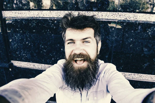 Hipster, τουριστικά tousled μαλλιά με μακριά γενειάδα που βλέπουν φωτογραφική μηχανή, λήψη selfie φωτογραφία. Vlogging έννοια. Ο άνθρωπος, τουρίστας με μούσι και μουστάκι σε χαρούμενο, χαμογελαστό πρόσωπο, μαύρο μάρμαρο φόντο — Φωτογραφία Αρχείου