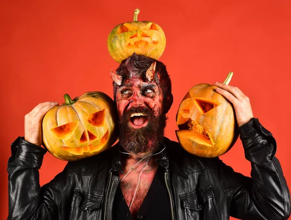 Man wearing scary makeup holds pumpkins on red background — Stock Photo, Image